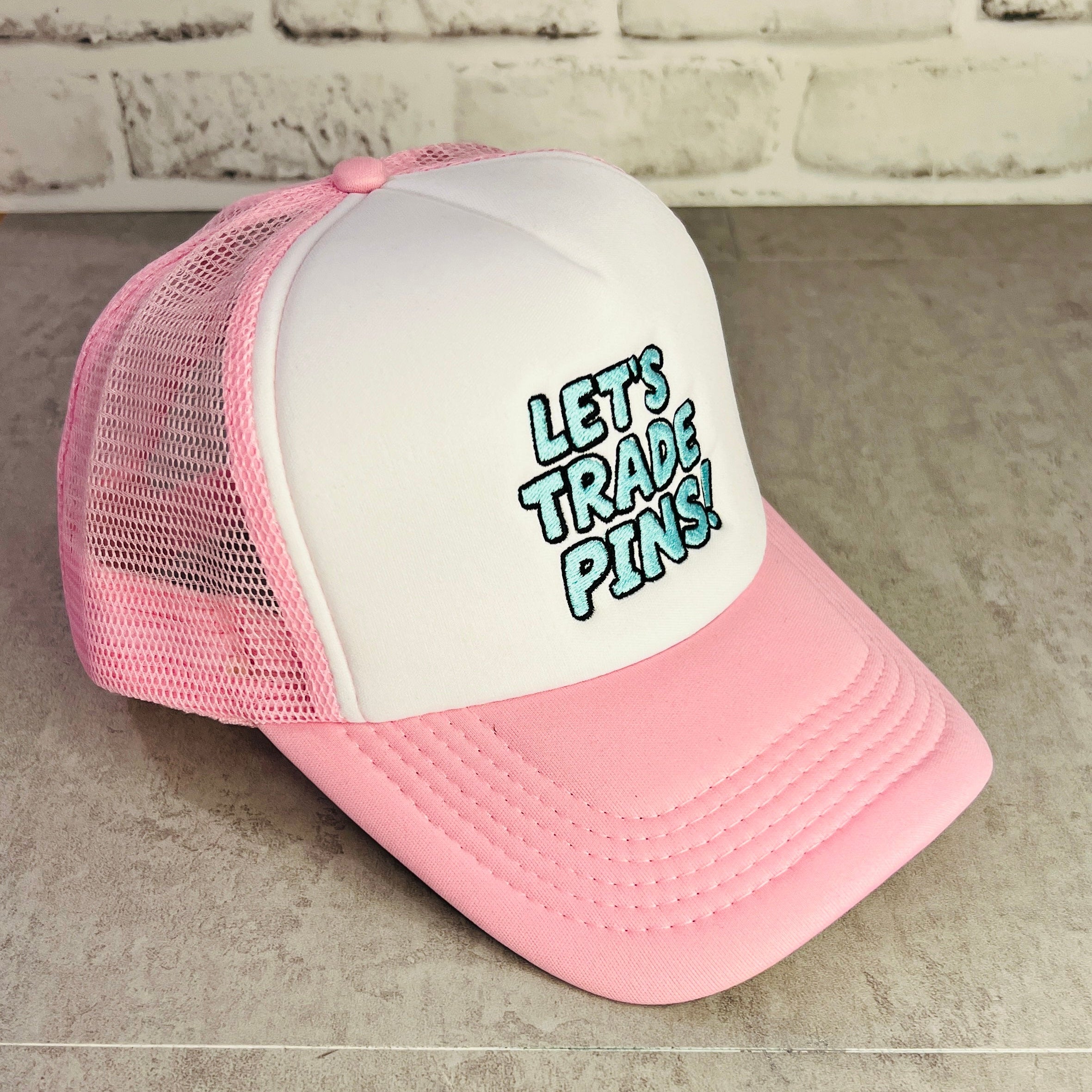 Pink and white trucker hat with 'Let's Trade Pins' text